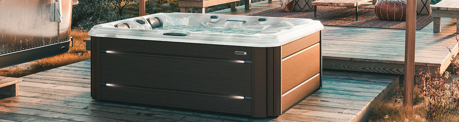 Rectangular outdoor hot tub with a white rim on a wooden deck at sunset, surrounded by outdoor seating.