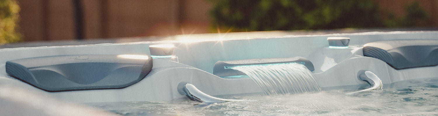 White hot tub interior with built-in seats and a small waterfall-like water feature cascading into the tub.