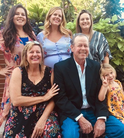 Smiling multi-generational family posing outdoors on steps, with greenery in the background.